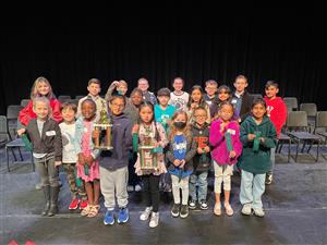 Group of students. Two in front one boy one girl from left to right hold trophies.